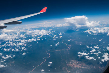 Fototapeta premium View from airplane window showing airplane wing with blue sky and white clouds