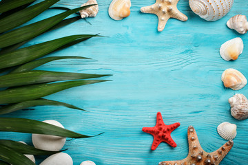 Sea stars, sea stones, palm leaves and shells lying on a blue wooden background . There is a place for labels.