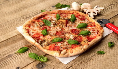 Hot and delicious pizza with salami tomatoes cheese and mushrooms ready to eat  on a wooden background.