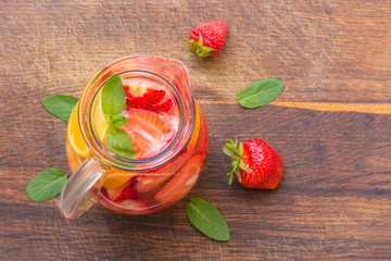 Aromatized water with fresh strawberries with oranges and mint in a glass jug .