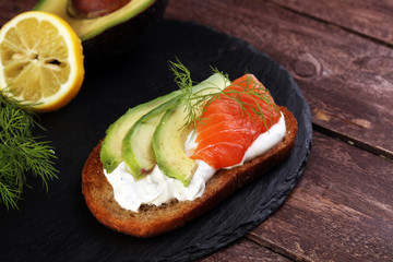 Bread with avocado and smoked salmon for lunch table. Sharing antipasti on party or summer picnic time over wooden rustic background.