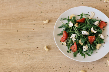 fresh salad with tomato, feta cheese, arugula, cashew on the wooden background