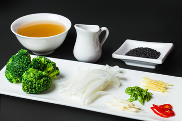 ingredients such as broccoli, onion, pep?er, garlic,sesames on the white plate on the black background