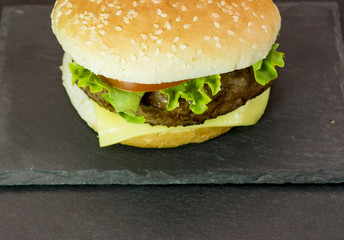 Delicious hamburger with cheese, lettuce and tomato on a stone