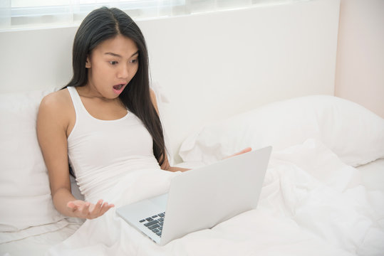 Asian woman looking to laptop on her bed.