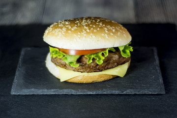 Delicious hamburger with cheese, lettuce and tomato on a stone