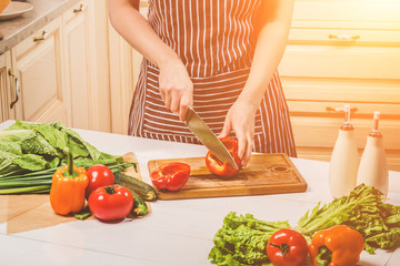 Young woman cooking in the kitchen at home. A woman cuts a pepper and vegetables with a knife.