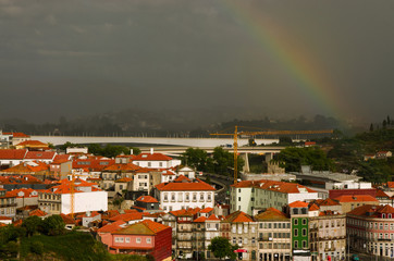 Tęcza nad miastem. Mocno zachmurzone niebo,  w dole oświetlone słońcem budynki. Miasto Porto...