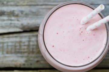 Strawberry pink smoothie in a glass with a straw on a old wooden rustic table. Summer and healthy lifestyle concept.