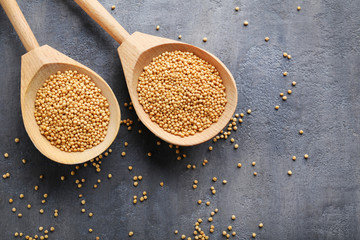Mustard seeds in wooden spoon on grey table