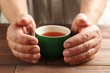 Hands of old senior with cup of tea on a wooden table