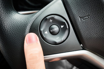 Close up of finger push on audio control on steering wheel in car