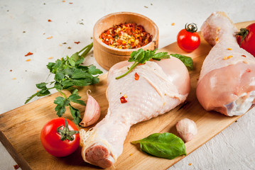Raw chicken legs. Meat, a source of protein. On a cutting board, on a white stone table. With spices, herbs and tomatoes for cooking. Copy space