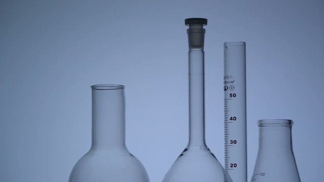 Tracking close-up shot of empty chemical glass flasks and test tube against gray background.