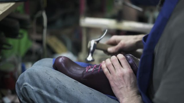 Cobbler hammering purple handmade woman shoe in a workshop and comparing it with the second one. Handheld real time close up shot.
