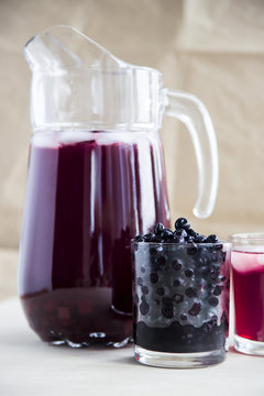 Blueberry juice in a decanter and a glass next to frozen berries