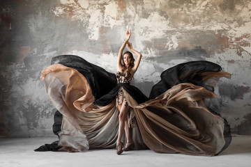 Beautiful woman in elegant dress waving on wind. Flying and fluttering dress over gray background....