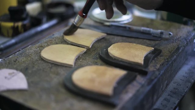 Close up of an unrecognisable shoemaker applying glue to a man s shoe heel on his table. Handheld real time close up shot