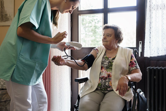Nurse measuring blood pressure of senior woman in elderly care home