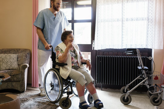 Elderly woman in wheelchair being helped by nurse getting out or her room in nursing home 