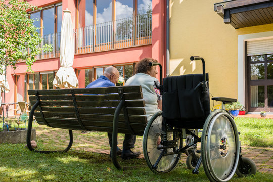 Senior man and woman in retirement home sitting on a bench in park