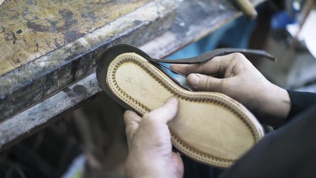 Close up of an unrecognisable shoemaker s hands cutting excessive leather making a shoe sole. Handheld real time close up shot