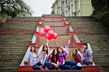 Group of six girls having fun at hen party, with balloons under rain at stairs of city.