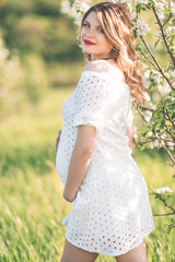 Happy pregnant woman in white blossom garden