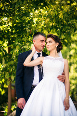 Beautiful couple walking in the park in their wedding day. Sunny weather.