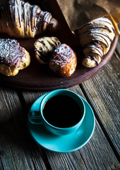 Croissant and white cup of black coffee on brown canvas.