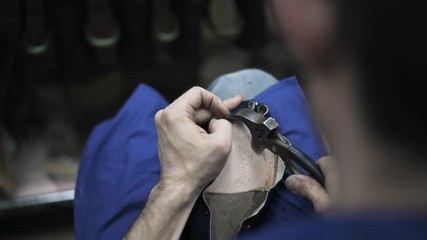 Close up of a shoemaker hammering nails into a blue shoe sole with pliers. Handheld real time close up shot