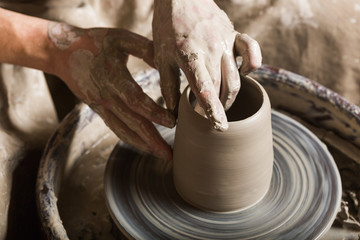 pottery, workshop, ceramics art concept - closeup on male hands sculpt some new utensil with fingers and water, man hands works with potter's wheel and raw fireclay, top view
