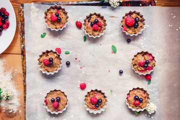 Top view Raw dough with berries for cupcakes decomposed into forms on a baking papper on baking tray decorated ewith flowers. Selective focus. Vintage concept, flatlay. Space for text