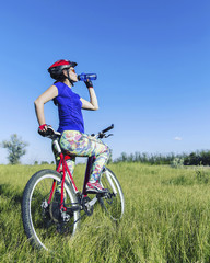 Obraz premium Attractive, healthy woman drinks from her water bottle on mountain bike. active outdoor lifestyle concept.