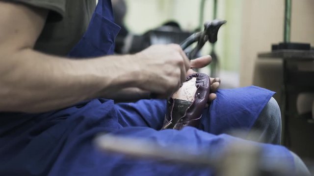 Side view of a shoemaker who glues leather to a shoe sole and removes pins with pliers. Handheld real time close up shot