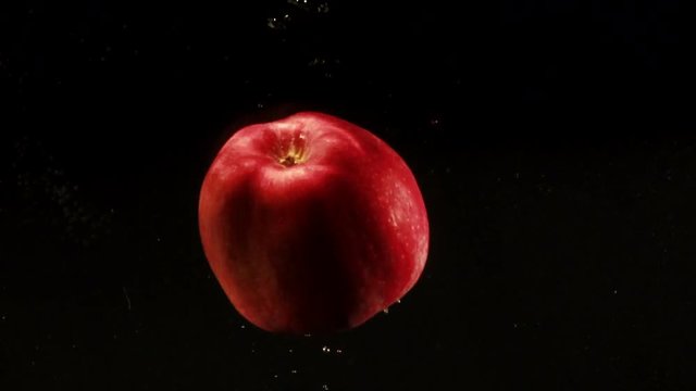 Red apples goes down and up in aquarium standing on black background
