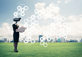 Camera headed woman standing on green grass against modern citys