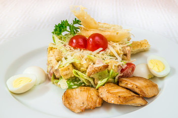 A tasty salad of vegetables, herbs and cheese, with boiled eggs and pieces of fried meat, on a white plate. Horizontal frame