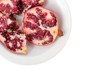 Broken red ripe pomegranates in white plate on white background