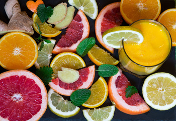 Beautiful composition of the lobules of  lemon, orange, mint, ginger, grapefruit, fresh orange juice in glass, on on black stone background. Top view. Concept of health, vitamin C. 