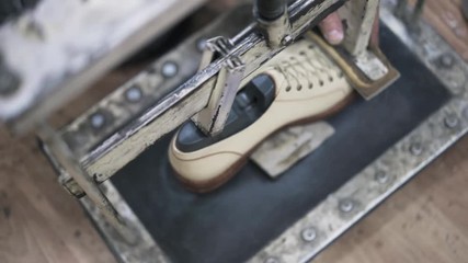 Close up of shoemaker s hands putting a loafer in a machine to let the glue dry. Handheld real time close up shot