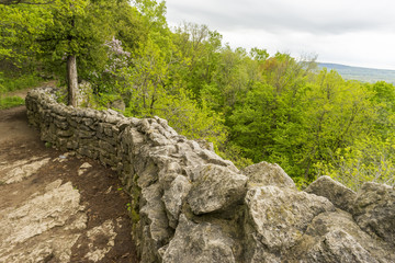 Fototapeta na wymiar Dirt footpath with old stone wall traveling along cliff edge with green forest and landscape views