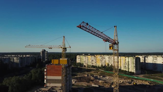 Industrial construction cranes and buildings over sun at sunset