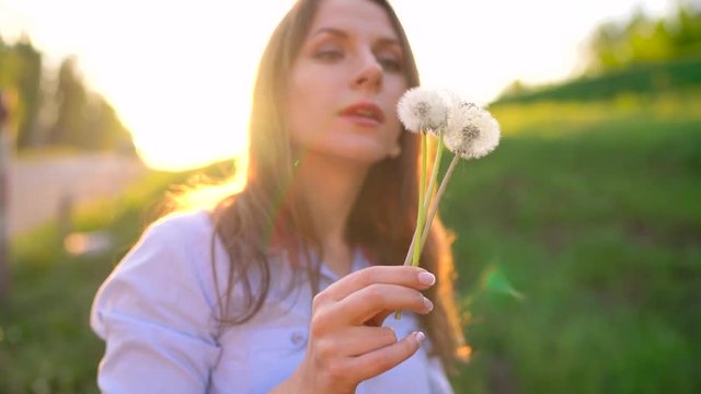 Beauty woman blowing dandelion against the sunset, slow motion