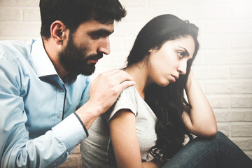 young woman looking away while man sitting behind her on the couch and consoling her