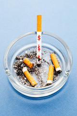 Stop Smoking - waste of money / dollars - with cigarettes and ashtray on blue background
