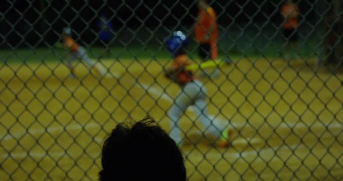 Slow motion from behind fence of kid batting and kid scoring at baseball game
