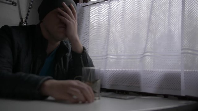 Man rides on the train, sitting at a table, window curtains closed. An alarmed look, an experience. He covers his face with his hand, worries looking at his smartphone, clasps his head with his hands