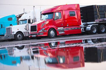 Big rig modern semi truck flat bed trailer with cargo on parking spot with reflection in water on parking lot