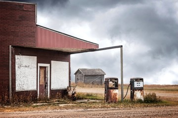 horizontal image of a very old abandoned gas station with two rusty broken down gas pumps under a...